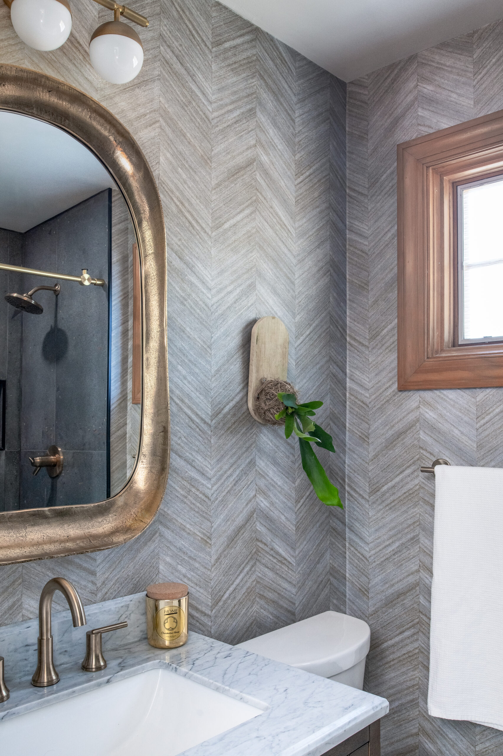 Looking into the corner, Plant mounted on wall Wallpaper on wall, Gold Oval Square Mirror, 3 globe light, dark vanity and gold plumbing fixture