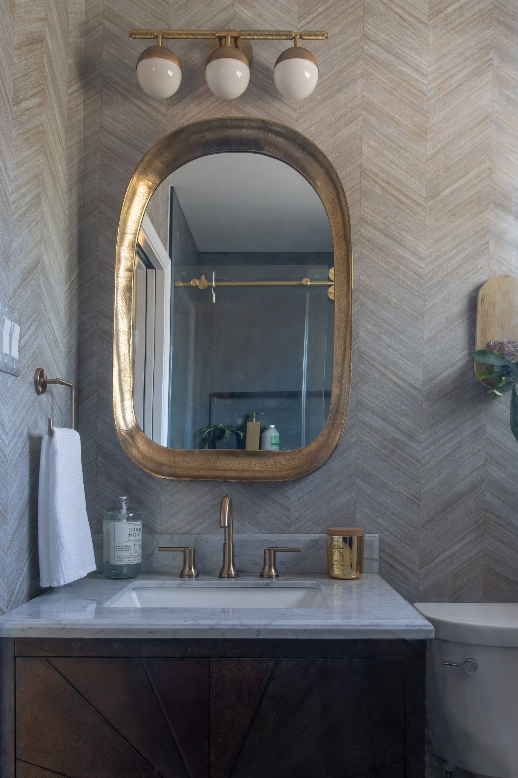 Wallpaper Wall, Gold Oval Square Mirror, 3 globe light, dark vanity and gold plumbing fixture