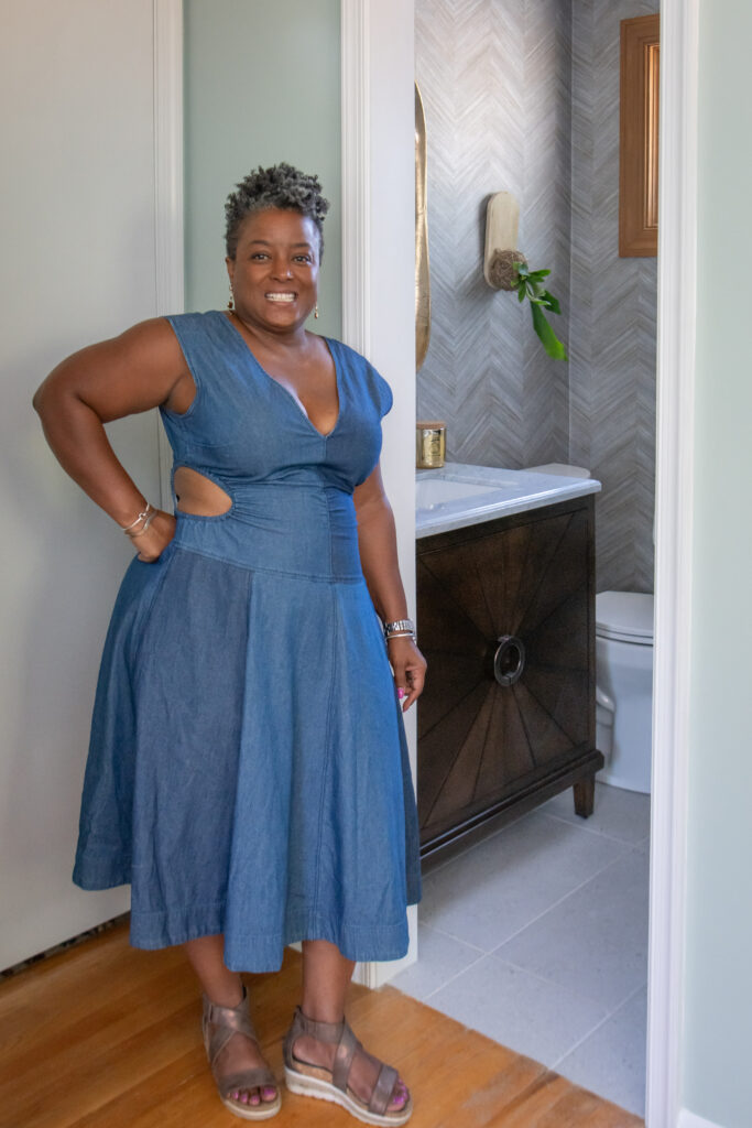 Sarah Wilson of Chansaerae Designs poses in front of bathroom door wearing a demin dress